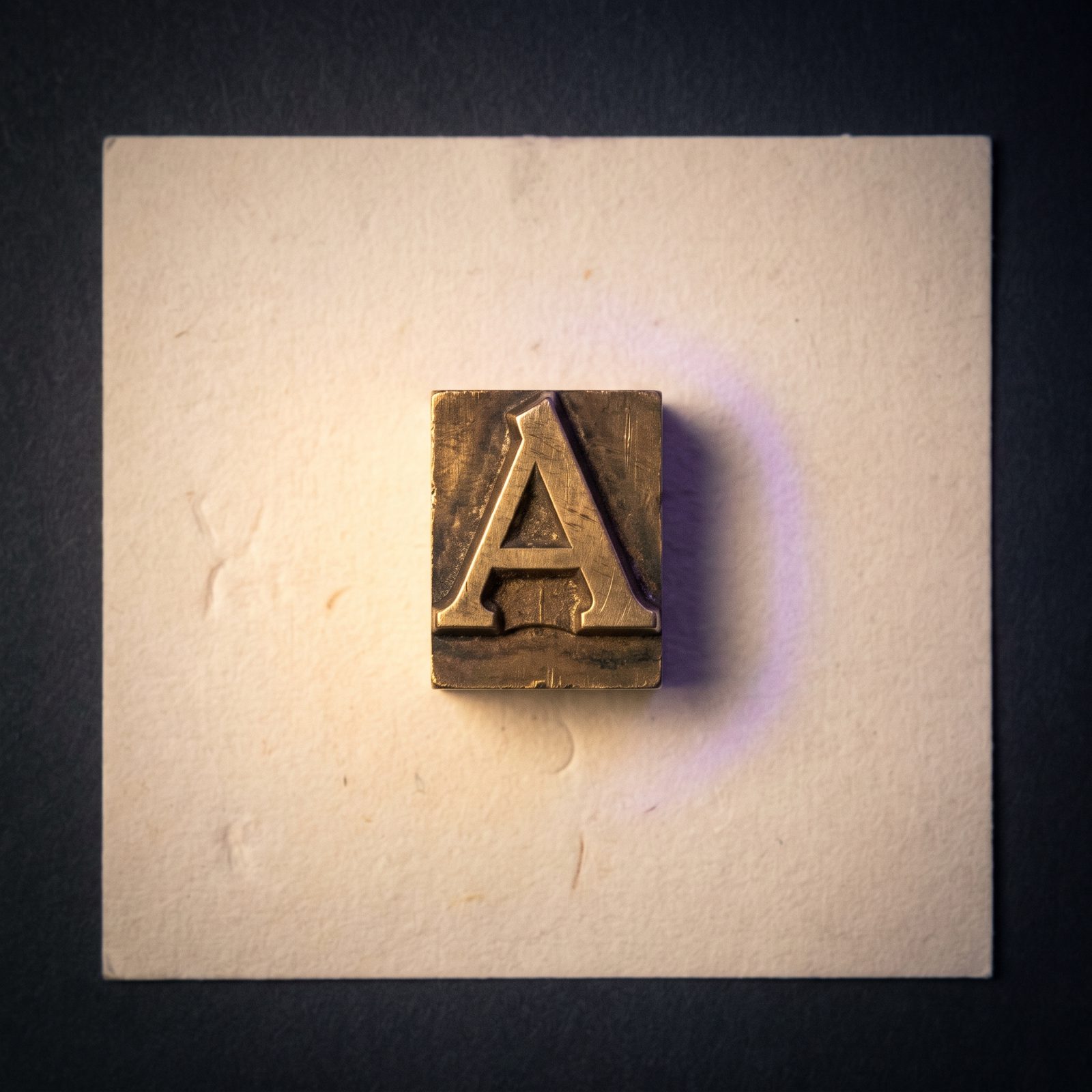 A single piece of hand-set metal type resting on cream linen